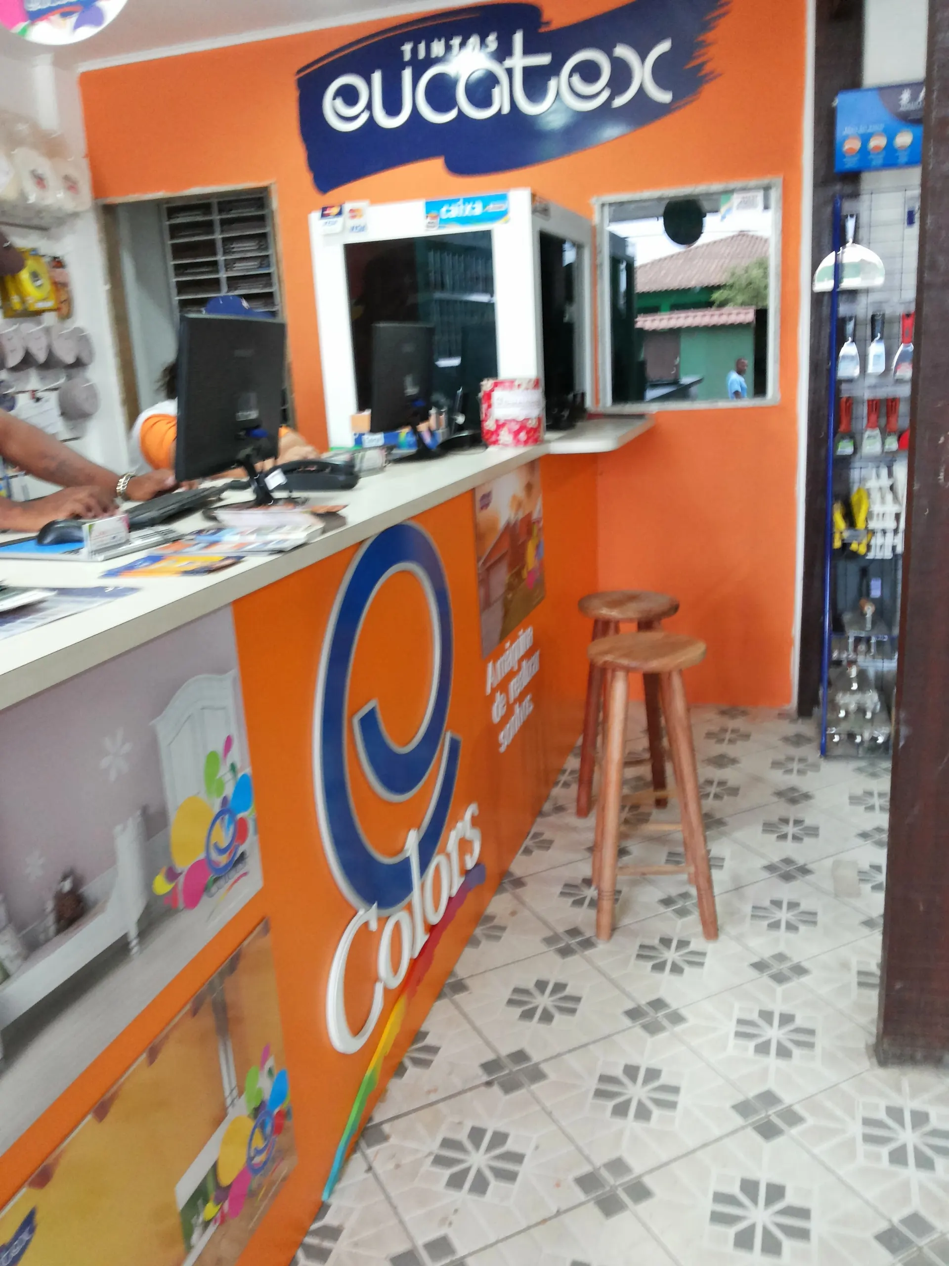 Balcão laranja de tintas com máquina tintométrica e leques de cores